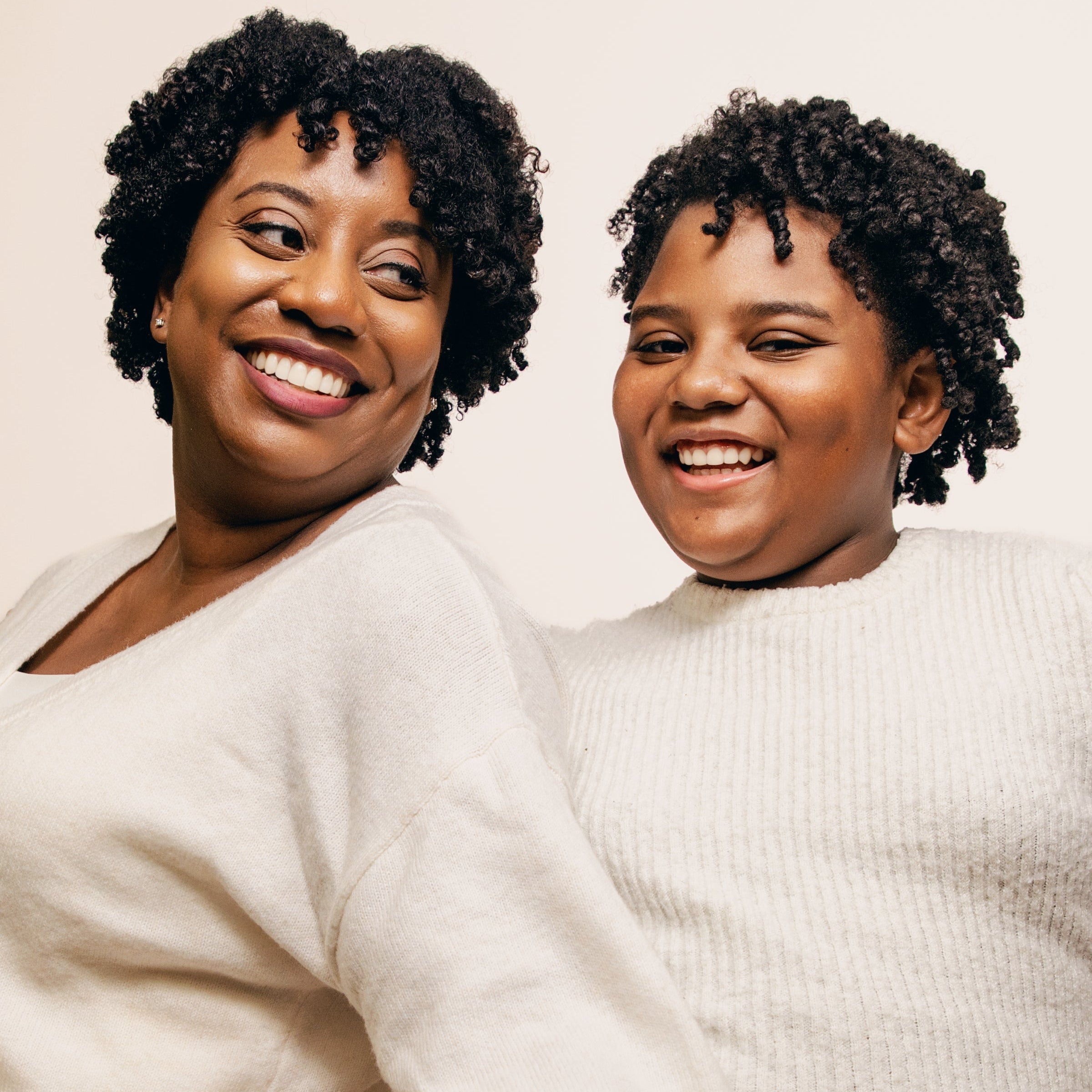 Two women with matching hairstyles and outfits sitting together against a plain background