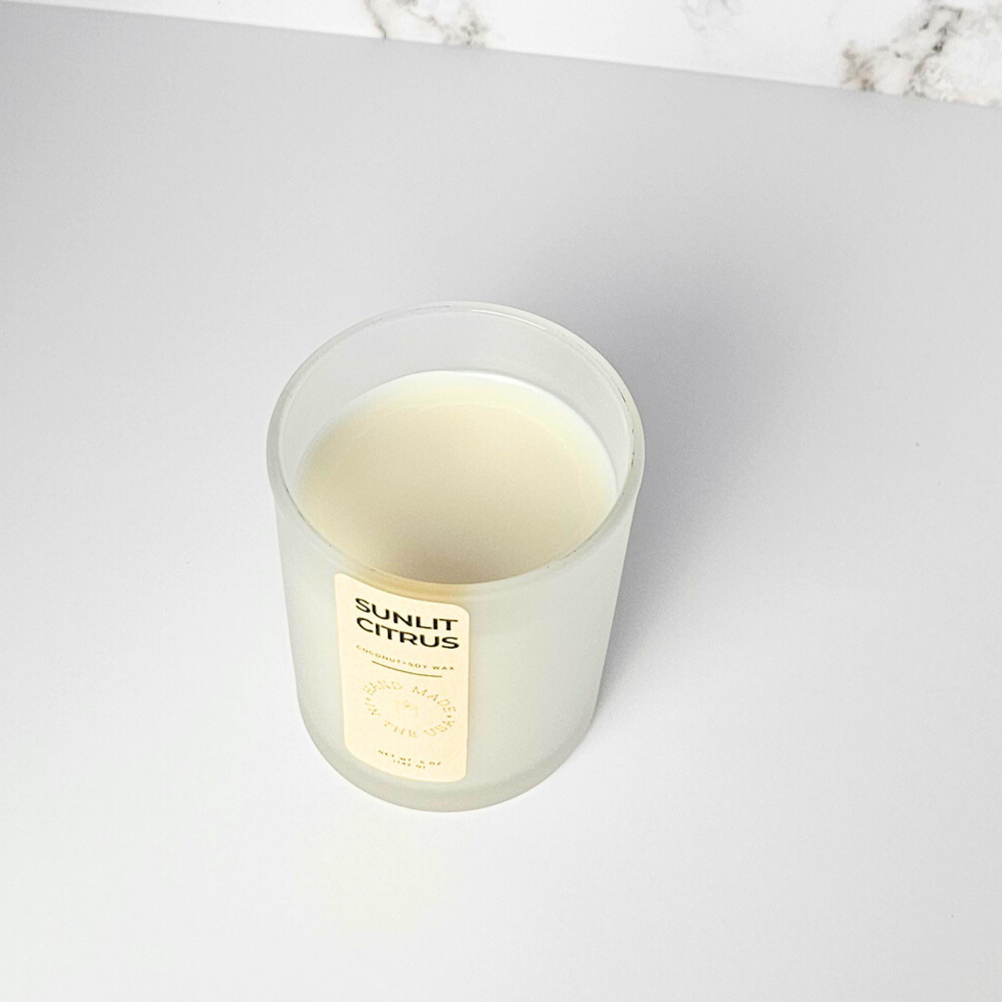 Candle labeled 'Sunlit Citrus' on a light gray surface