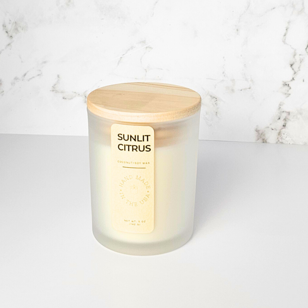 Candle labeled 'Sunlit Citrus' with a wooden lid on a marble background