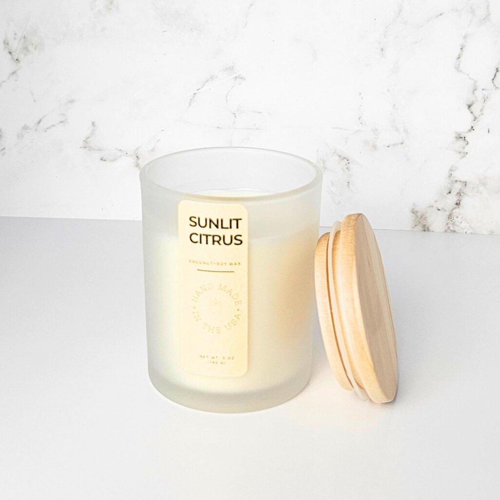 Candle labeled 'Sunlit Citrus' with a wooden lid on a marble surface